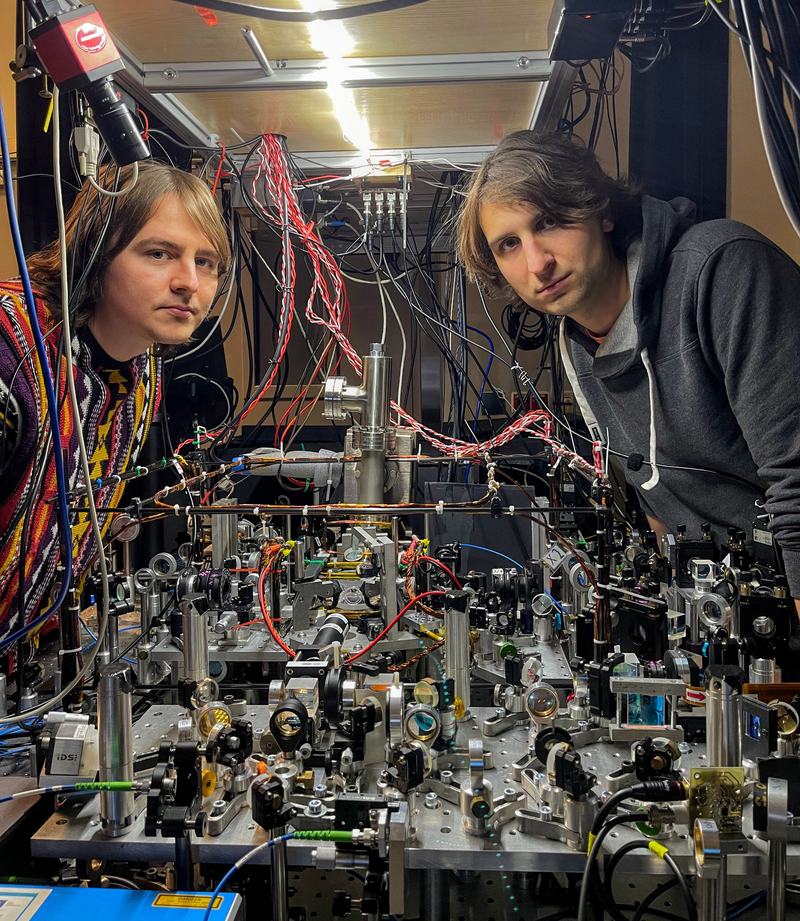 Two researchers look into the camera from behind a densely built optical setup